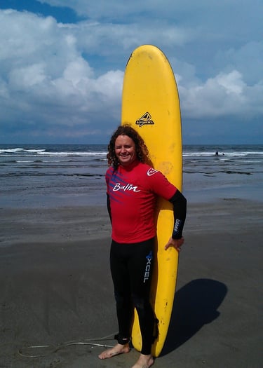 Surf school owner Gray satnding with a yellow surfboard behind him at the beach