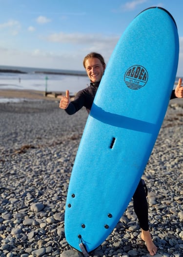 Surf coach Celynholding a blue surfboard and giving a double thumbs up