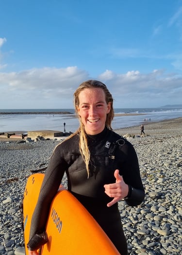 Surf coach Cerys holding an orange surfboard and giving a shaka