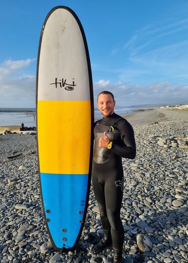 Surf coach Matt, holding a Tiki Grizzly surf board and giving the thumbs up