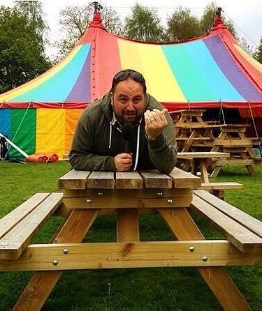 Wynne Evans lying on a picnic beach with a colourful circus tent in the background