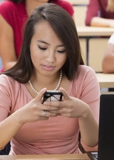 a woman sitting at a desk with a laptop and a cell phone