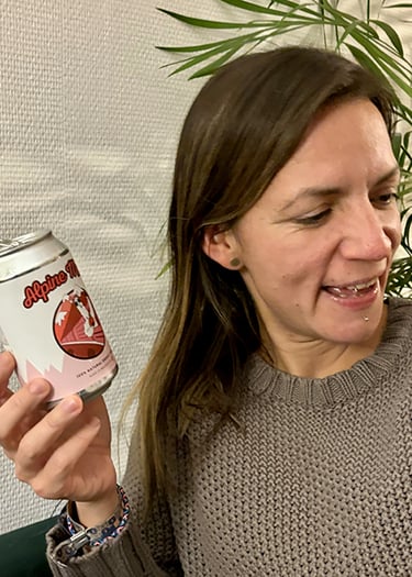 Une femme en pull gris tenant une canette de boisson énergisante naturelle Alpine Mate