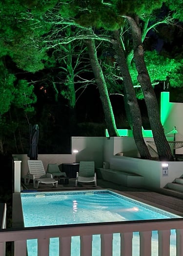 The photograph depicts an illuminated pool and part of the courtyard of Lokva Rogoznica's house.