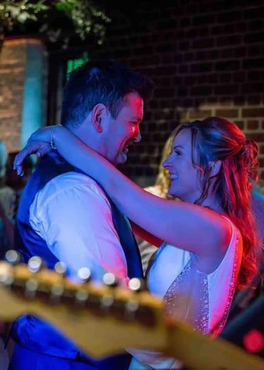 A smiling bride and groom enjoy their first dance at a rustic indoor wedding reception.
