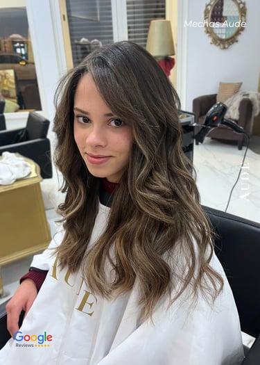 Young woman with long brunette hair and honey blonde balayage highlights styled in loose waves at a salon.