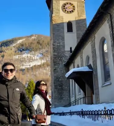 Tourists walking past the historic church tower in Zermatt village center as part of a cultural walk