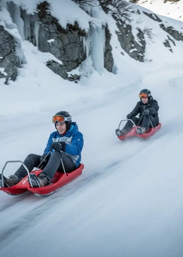 Two people in winter gear sliding down a snowy hill on red plastic sleds during a winter vacation.