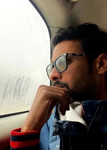 a man named Alok Dinesh in a blue jacket and sunglasses sitting in a car
