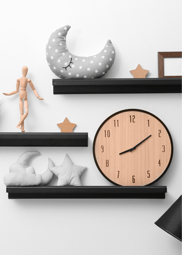 Wall decor featuring black floating shelves with a wooden clock, moon pillows, and stars.