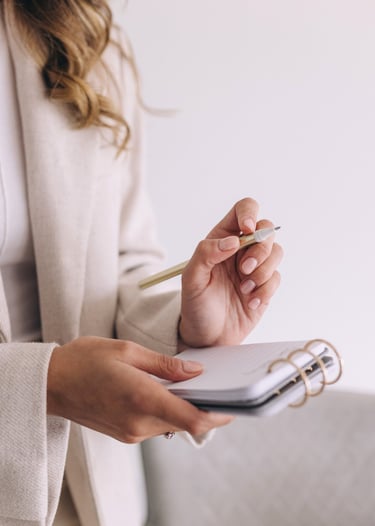 a woman in a white suit holding a notebook and a pen