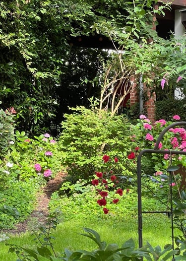 Ein Garten mit bunten Blüten im Sonnenschein vor einem Hauseingang.