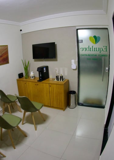 Modern clinic waiting room with green chairs, wooden cabinet, and wall art in a wellness center.