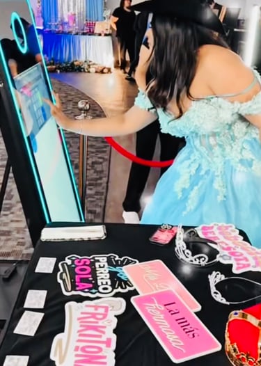 Girl in a blue dress at a Quinceañera interacting with a Mirror Photo Booth with props on the table.