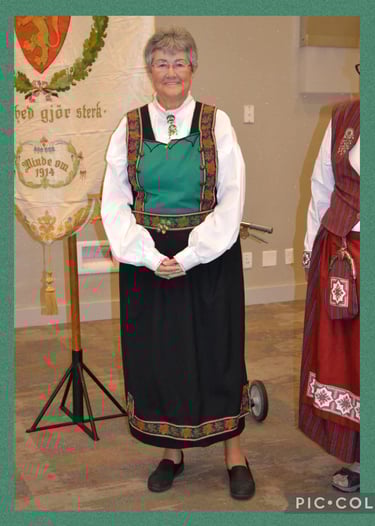 a woman with glasses in a grean and dark blue Tinn bunad