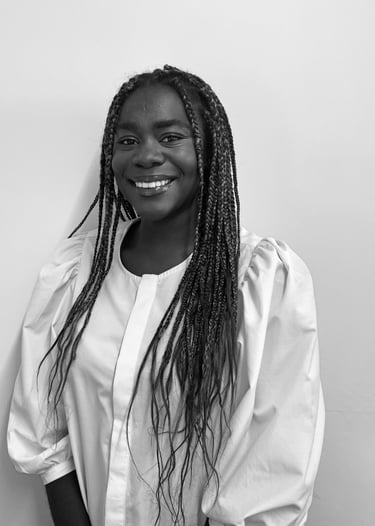 Smiling Black woman with long braids wearing a puff-sleeve white blouse in a black and white portrait.