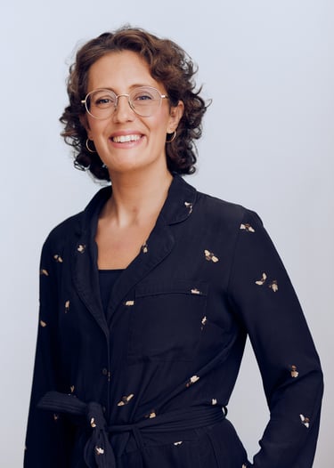 Woman in a dark blue jumpsuit wearing glasses.