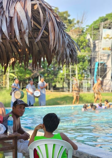 Guests relax by a tropical swimming pool during a live music performance with traditional dancers.