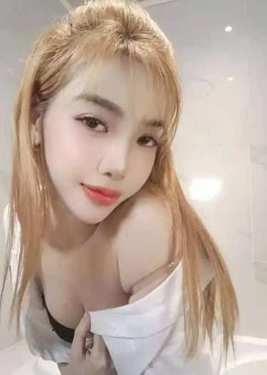 A blonde woman with red lipstick posing in a white button-down shirt in a modern bathroom.