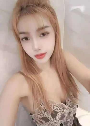 A young woman with long blonde hair wearing a lace-trim black camisole poses for a selfie.