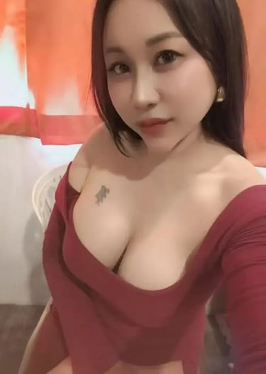A young woman with dark hair and a small chest tattoo wearing a low-cut red long-sleeve dress.