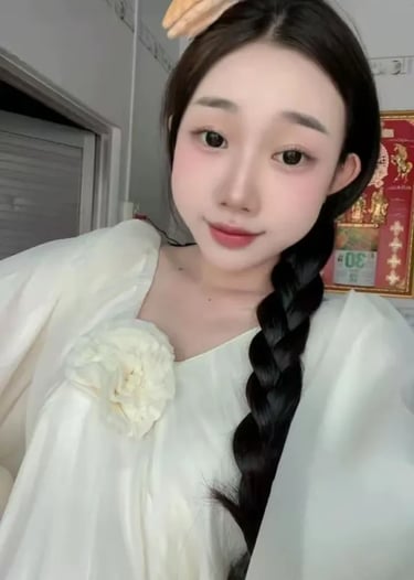 Young woman with long black braided hair wearing a white blouse with a floral brooch and a cute cookie hair clip.