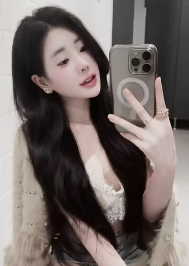 Young woman with long dark hair taking a mirror selfie wearing a lace top and fuzzy cardigan.