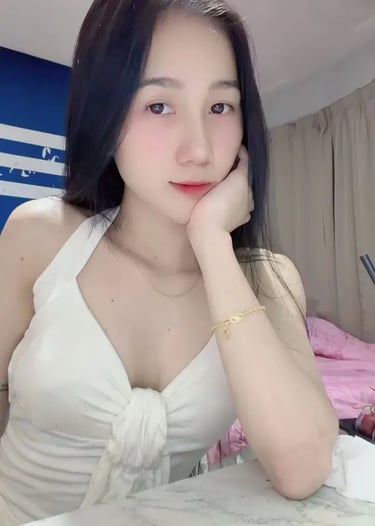Young woman with long dark hair wearing a white halter top posing indoors at a marble table.