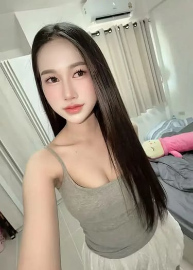 Young woman with long dark hair taking a selfie in a grey tank top and white skirt indoors.