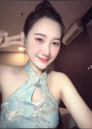 A smiling young Asian woman in a light blue floral halter dress making a peace sign.