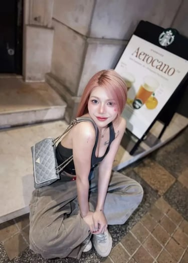 A stylish young woman with pink hair wearing cargo pants and a designer shoulder bag posing outdoors.