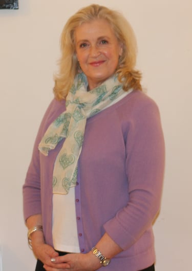 blonde haired woman smiling wearing light purple cardigan and green scarf