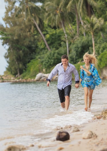 A happy couple holding hands and running along a tropical beach on Koh Samui, Thailand