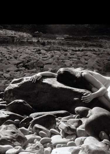A woman holding and being held by smooth solid rocks surrounded by smaller rock fragments