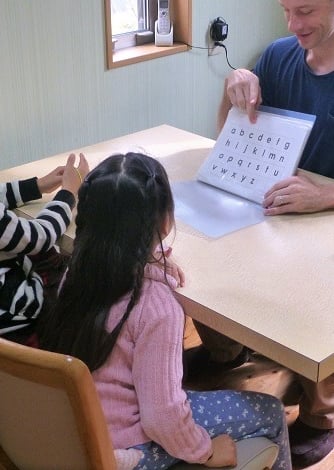 an English teacher and girls sitting at a table practicing ABCs