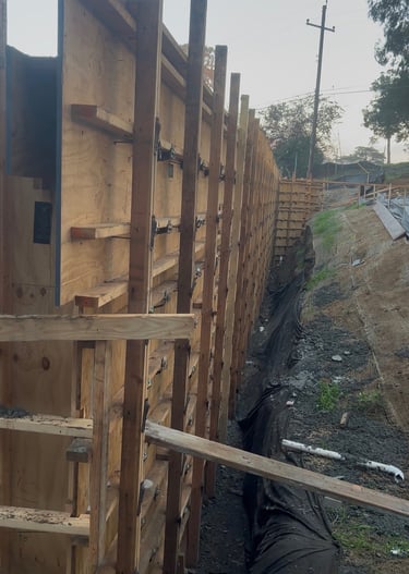 A long wooden retaining wall formwork construction site with plywood panels and timber bracing.