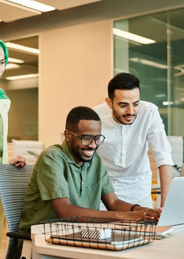 one male colleague seated at laptop and female and male colleague look at screen with him.