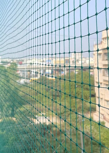 An installer carefully fitting a safety net on a high-rise balcony overlooking Basavanagudi streets.