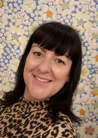 a woman with dark hair and a fringe wearing leopard print standing against a floral background