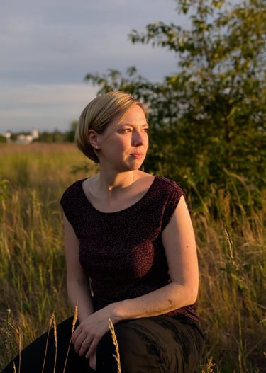 Grabrednerin kniet auf einer Wiese und schaut in den Sonnenuntergang in Falkensee