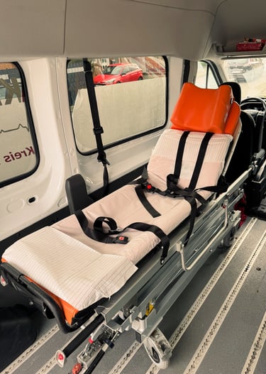 Trage im Rettungswagen mit orange Kopfstütze, rotes Auto draußen.