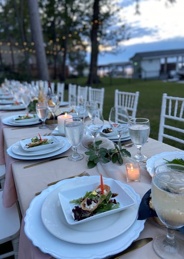 Outdoor al fresco dining table with plates, napkins and cutlery neatly arranged. Candles and flowers