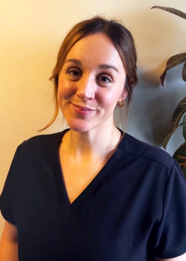 A smiling female healthcare professional wearing navy blue medical scrubs standing indoors.