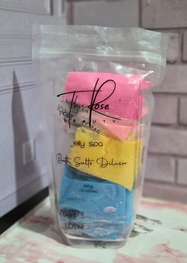 A clear bag of The Rose Beauty Jelly Spa bath salt dilutor packets in pink, yellow, and blue colors.