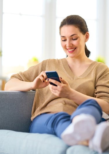 Smiling woman using a smartphone while relaxing on a sofa while waiting for her mobile mechanic.