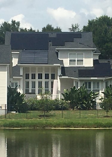 Modern suburban home with residential solar panels installed on a shingle roof near a lakeside.