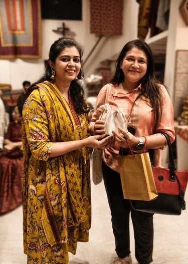 Two women smiling while holding a small fabric gift bag at a traditional Indian clothing boutique.