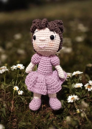 Muñeca amigurumi de ganchillo hecha a mano, vestido morado, de pie en un campo de margaritas blancas