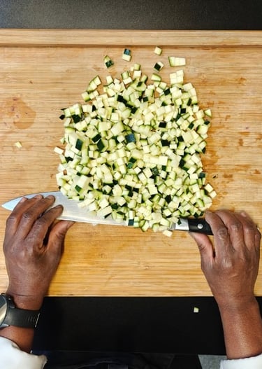 Chef Viviane's hands chopping courgette into fine dice with a chef's knife, top-down view