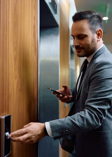 a man in a suit and tie is holding a cell phone and pushing the elevator button to request a ride